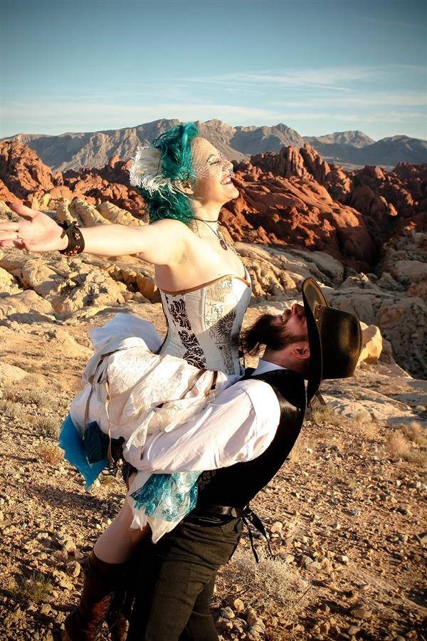 Steampunk groom lifting blue haired bride in the desert sunshine