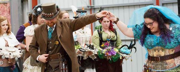 Steampunk bride and groom, with bridesmaids watching on.